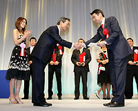 ワシントンの代理で受賞した浦和レッズ・藤口光紀社長（右）にハイオクガソリン１０００リットルの目録を渡す昭和シェル石油・村山康夫代表取締役社長と同イメージパーソナリティーの牧野紗弥さん（左）