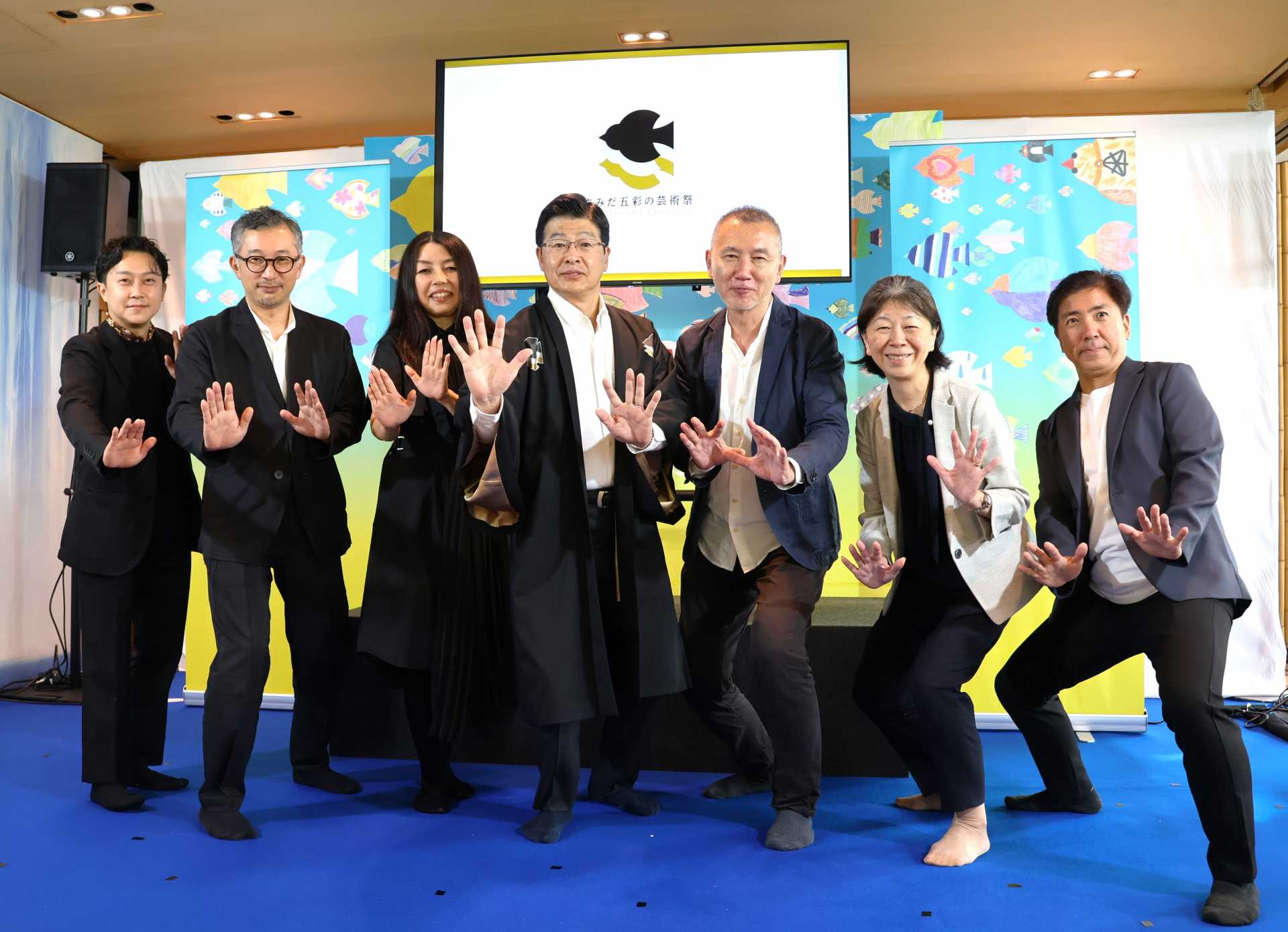東京・両国の回向院で会見を行い、相撲のポーズを取る墨田区・山本亨区長（中央、同右は神野真吾エグゼクティブディレクター、右からディレクターの清宮陵一氏、荻野康子氏、左から青木彬氏、三田大介氏、デザイナーの髙橋正実氏）